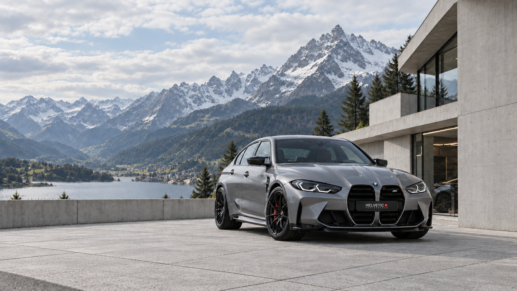 BMW M3 G80 argentata davanti a un’architettura svizzera contemporanea con vista su un lago alpino.